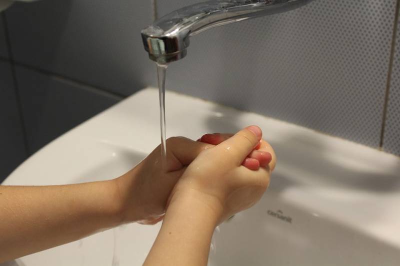 A child washes their hands under a silver tap to stop spreading germs