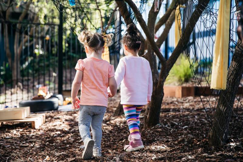 Two children hold hands walking across a play area thinking about their next fun projects for kids.