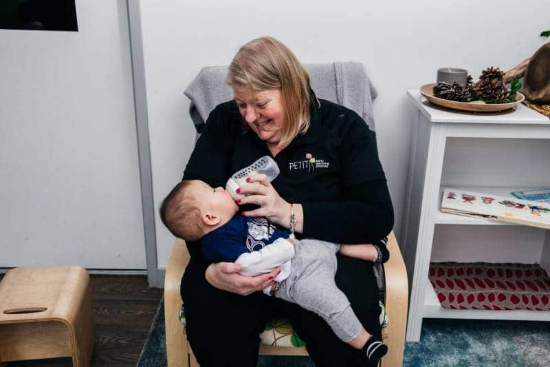 Educator cuddles a baby in the nursery while providing essential fluids for hydration - a good tactic for pain management.