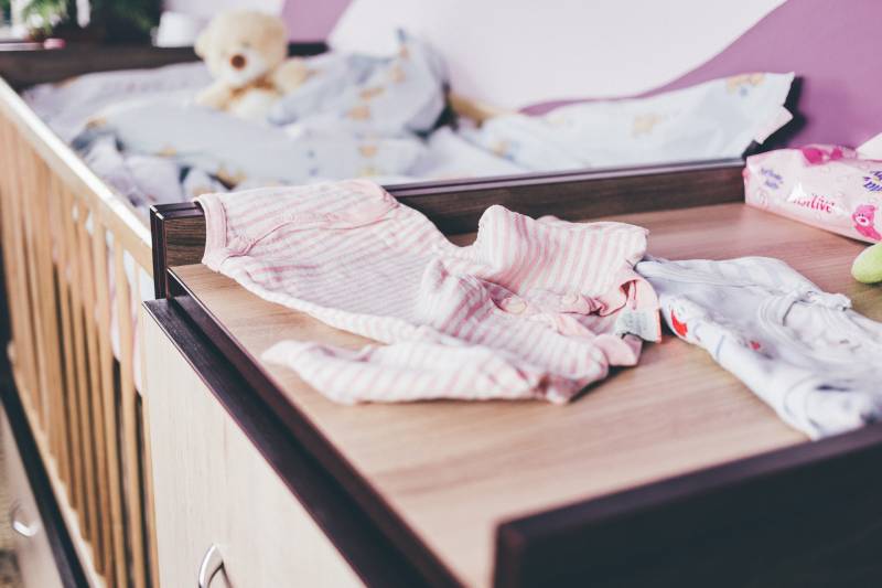 Teddy bear sits on a cot behind a change table with baby accessories.