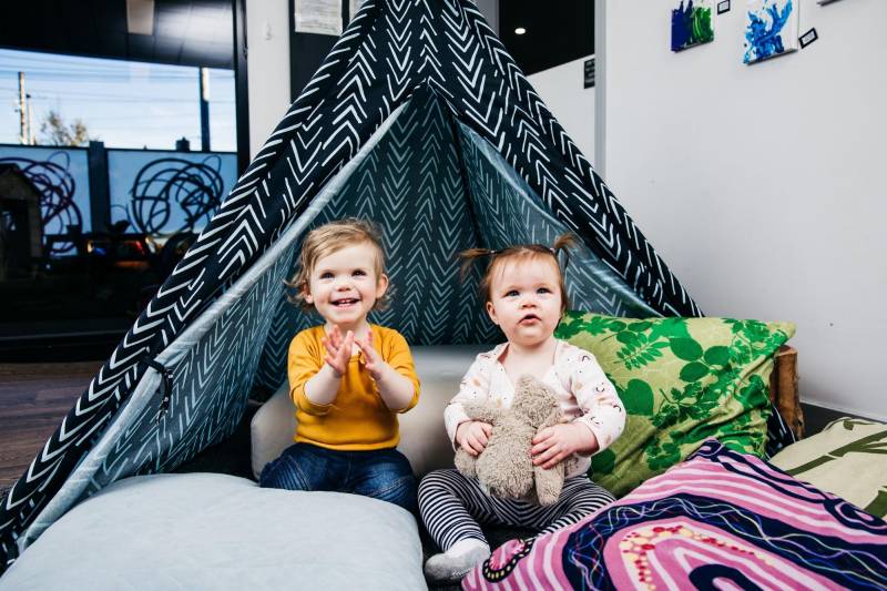 Two children sit inside a teepee play tent surrounded by cushions a cool, kids party theme.